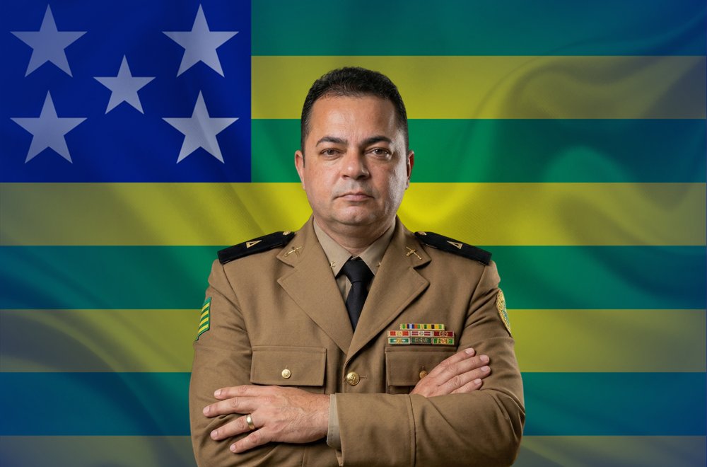 Subtenente Sérgio fardado, de braços cruzados, à frente da bandeira de Goiás